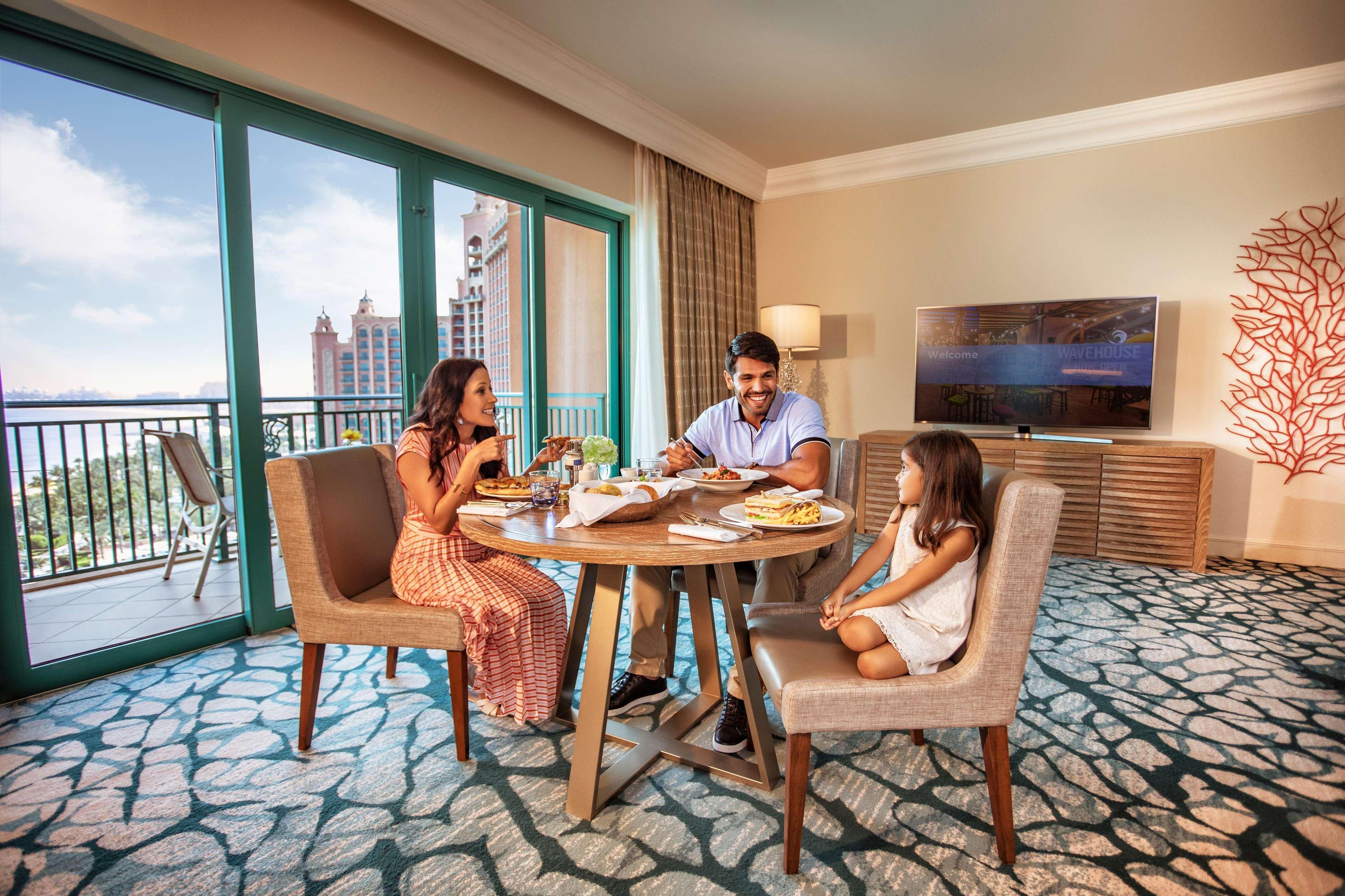Atlantis, The Palm Dubai Exterior foto The image shows a family dining together in a modern, well-furnished hotel room. There are three people around a round table: an adult male and female, and a young girl. They appear to be enjoying a meal, with various dishes set out on the table. Beh